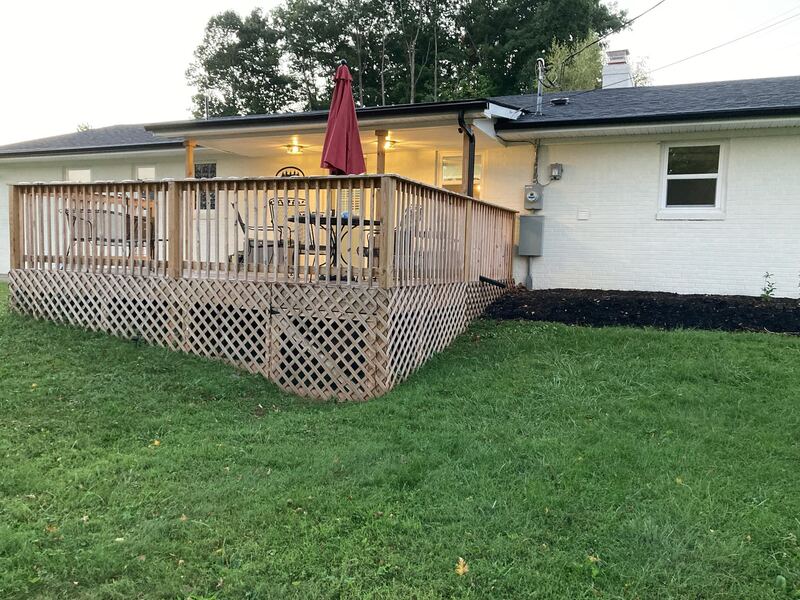 The back of the house at dusk, showing the raised timber deck with lattice skirting and the covered rear porch with its lights on.
