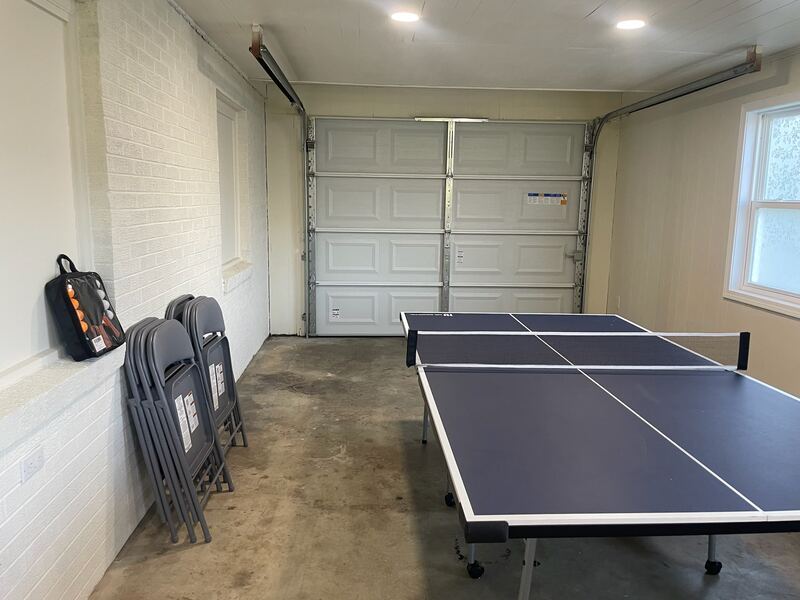 The garage set up as a games room, with a full-size ping pong table, painted brick walls, and folding chairs stacked against the wall.