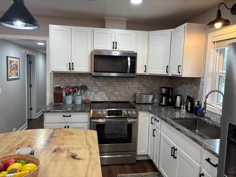 The kitchen, with white shaker cabinets, a patterned tile backsplash, dark granite counters and stainless steel appliances.