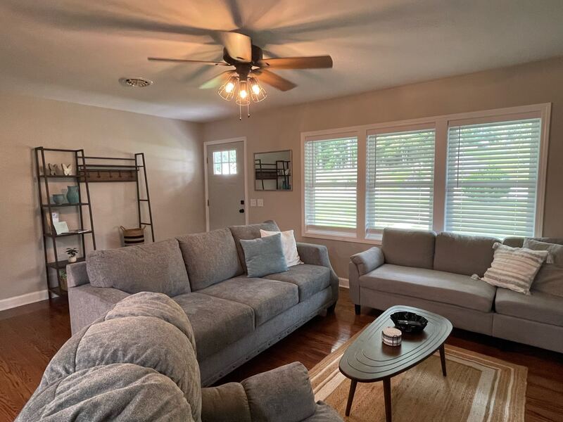 A second seating area by the front door, with a grey sectional and loveseat, and a ladder-style shelf and coat rack against the wall.